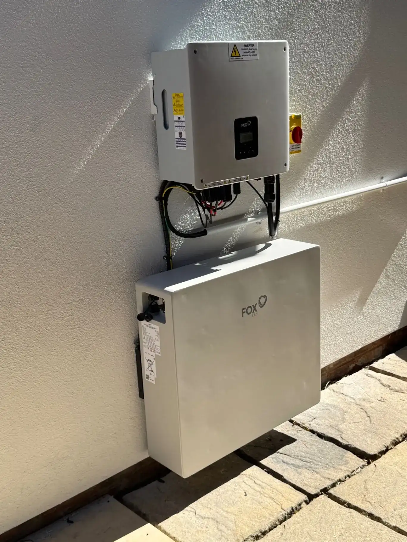 Wall-mounted inverter above a white battery storage unit with visible cabling