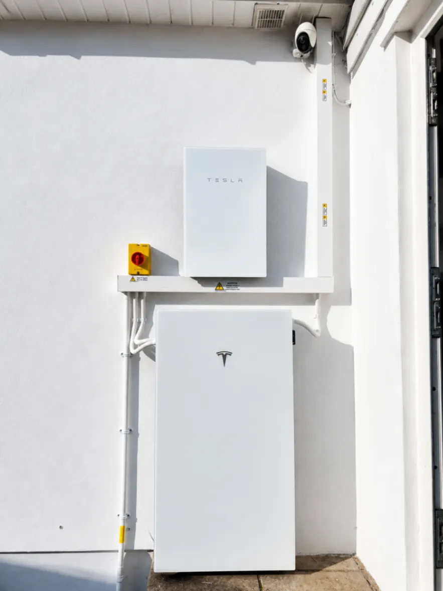 White wall-mounted battery and inverter system with a red isolator and conduit